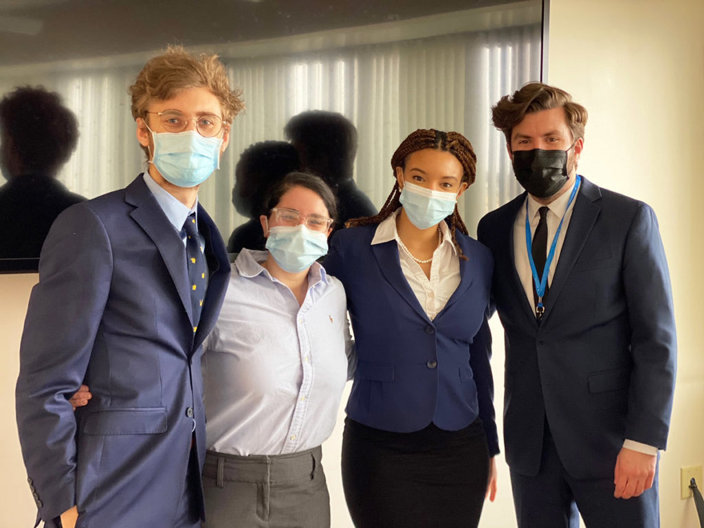 Photo of team members Samuel Jump, Josheili Llavona-Ortiz, Bukola Toyobo and Dr. Ryan Holcomb standing and taking a break after presenting their plan to judges.