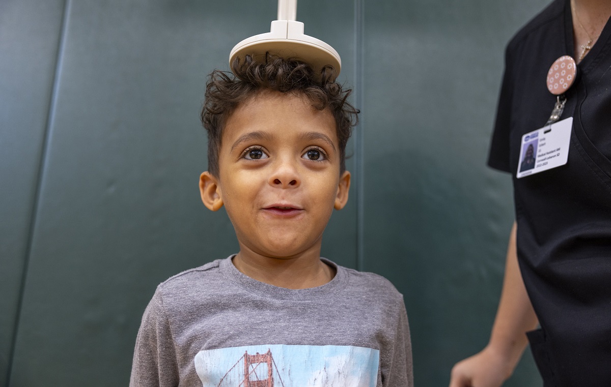 A little boy stands as a health care worker puts a disk on top of his head to measure his height.