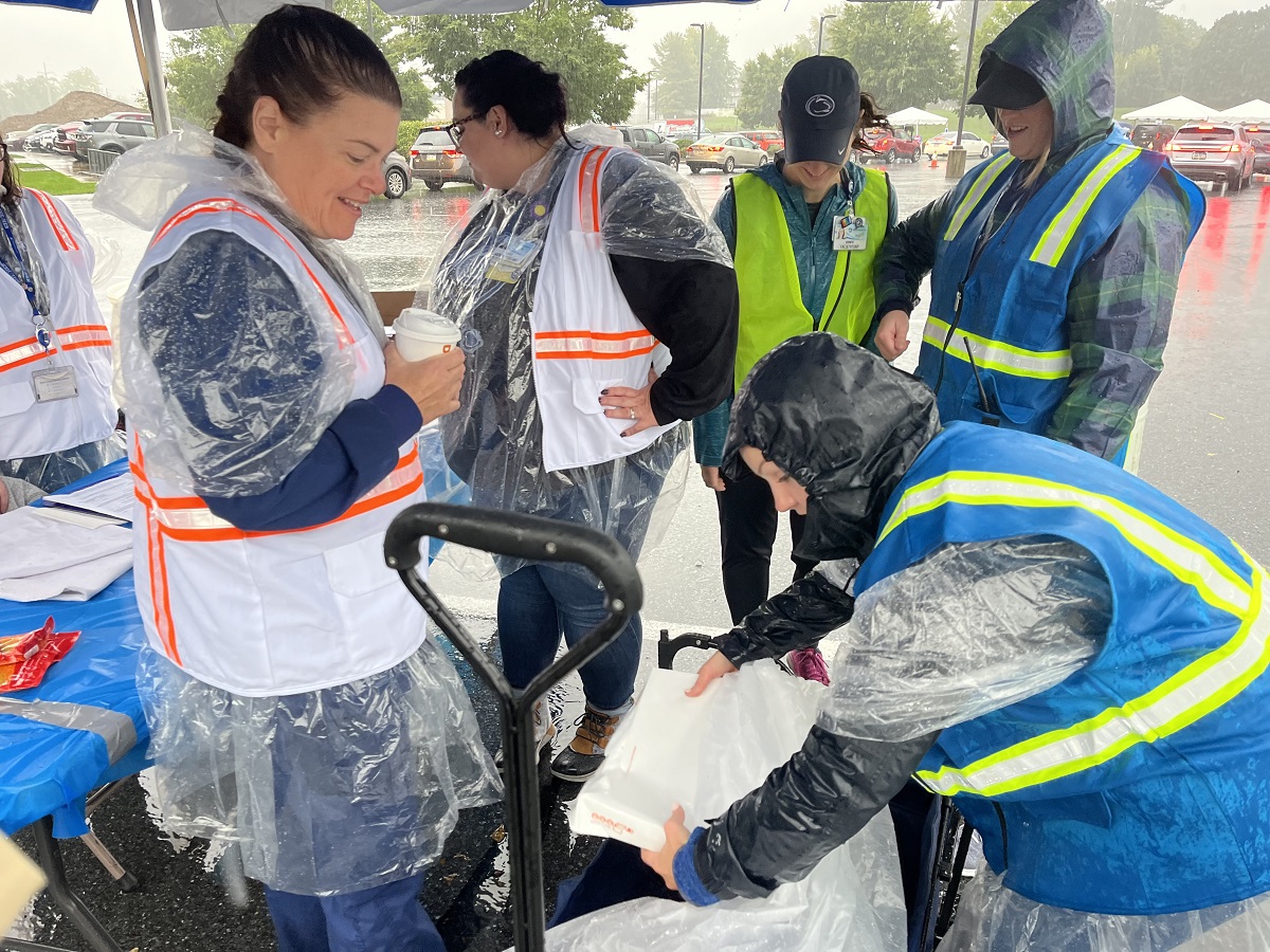 A group of people in ponchos drink coffee and unload boxes under a tent.