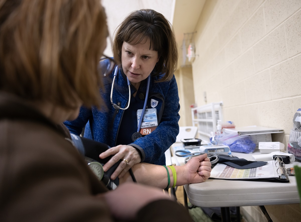 A woman with a stethoscope wraps a blood pressure cuff around the arm of a woman facing her.